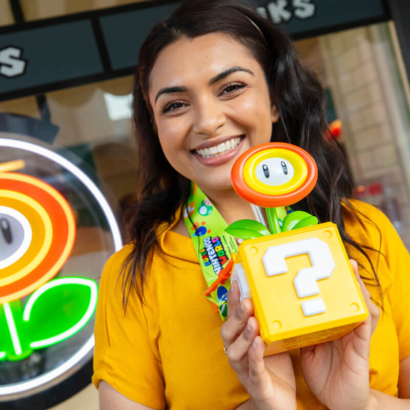 A smiling teen holds up her SUPER NINTENDO WORLD™ Fire Flower Sipper souvenir cup.