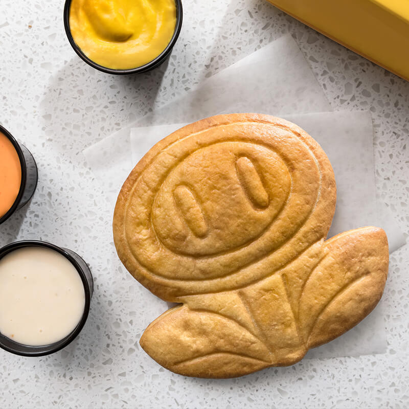 A SUPER NINTENDO WORLD™ Fire Flower themed pretzel alongside various dipping sauces.