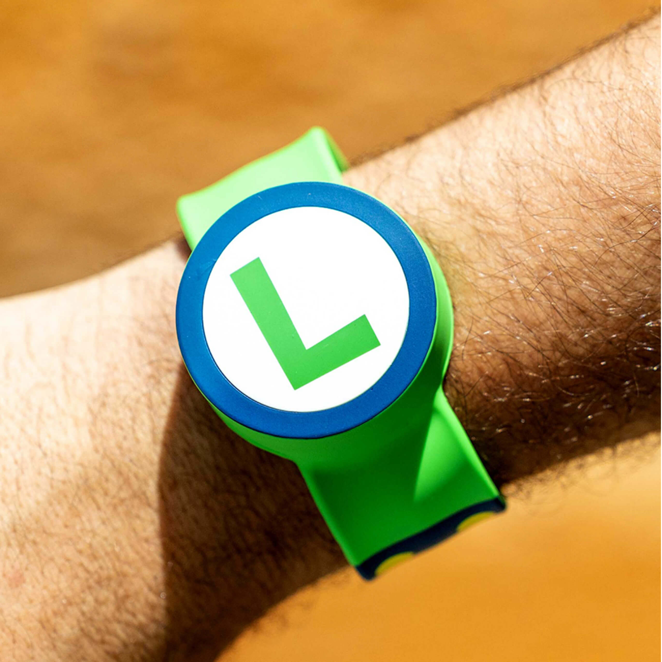 An arm wearing a Power-Up Band on its wrist. On the band is the letter ‘L’ representing the Super Mario character Luigi.