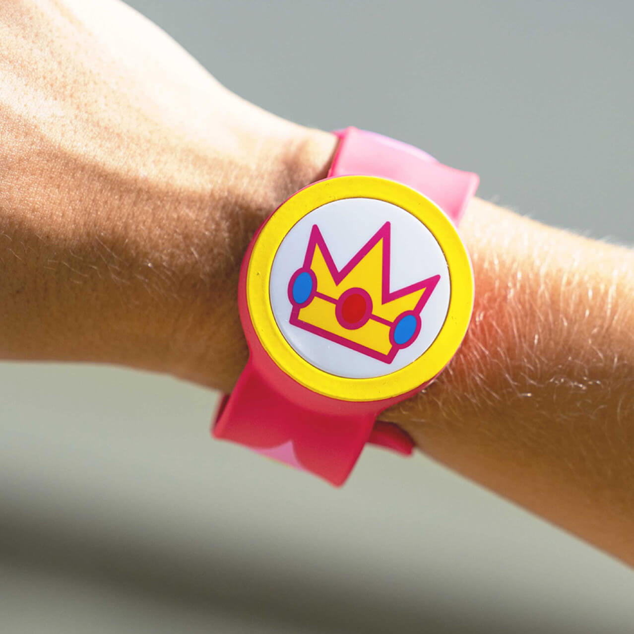 An arm wearing a Power-Up Band on its wrist with a crown symbol representing the Super Mario character Princess Peach.