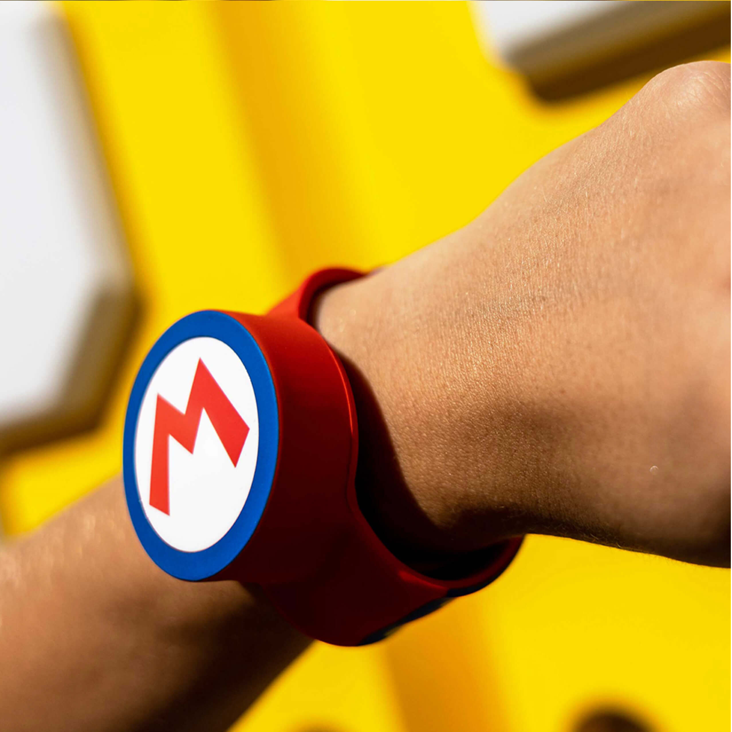 An arm wearing a Power-Up Band on its wrist. On the band is the letter ‘M’ representing the Super Mario character Mario.
