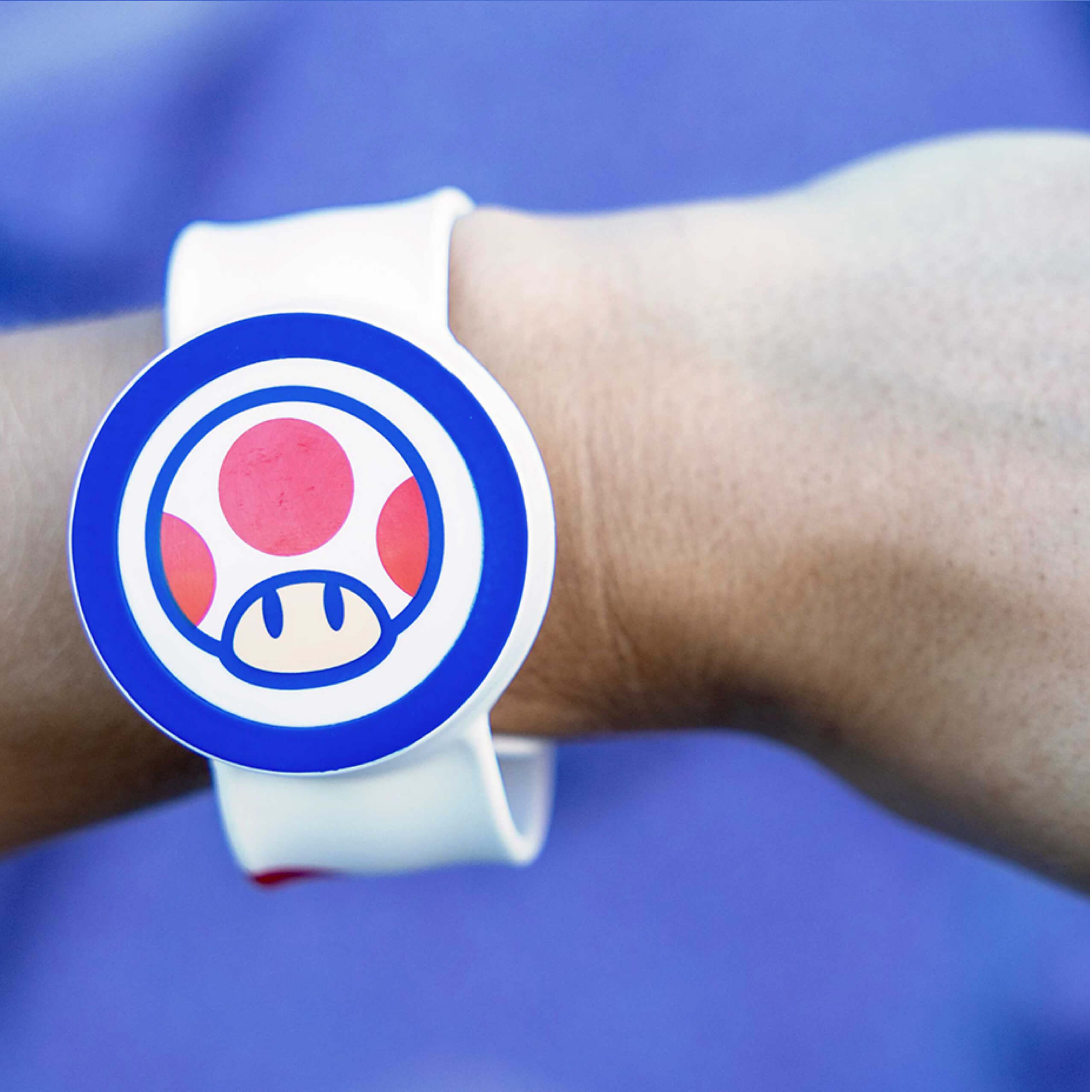 An arm wearing a Power-Up Band on its wrist with the face of the Super Mario character Toad.