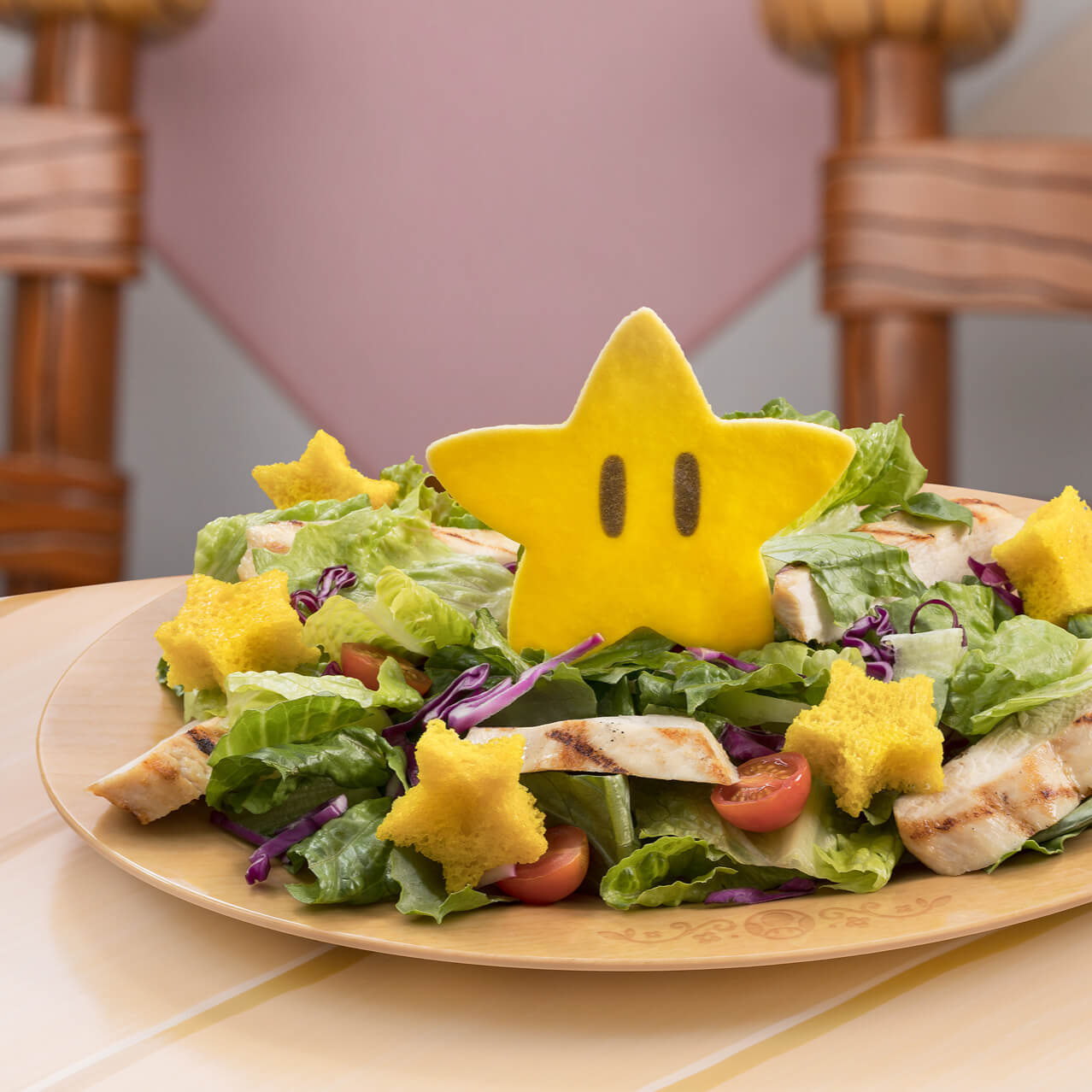 A plate featuring a salad with greens, grilled chicken strips and yellow star-shaped croutons. A large parmesan Super Star sits in the middle of the salad.