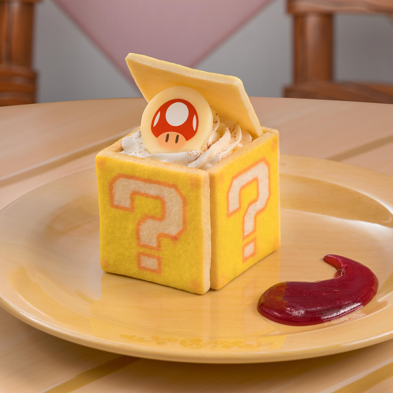 A plate with a tiramisu pastry shaped like a “question box” from the Super Mario™ games. There are question marks on the sides, and atop the open box sits a white chocolate coin with the image of a Super Mushroom.
