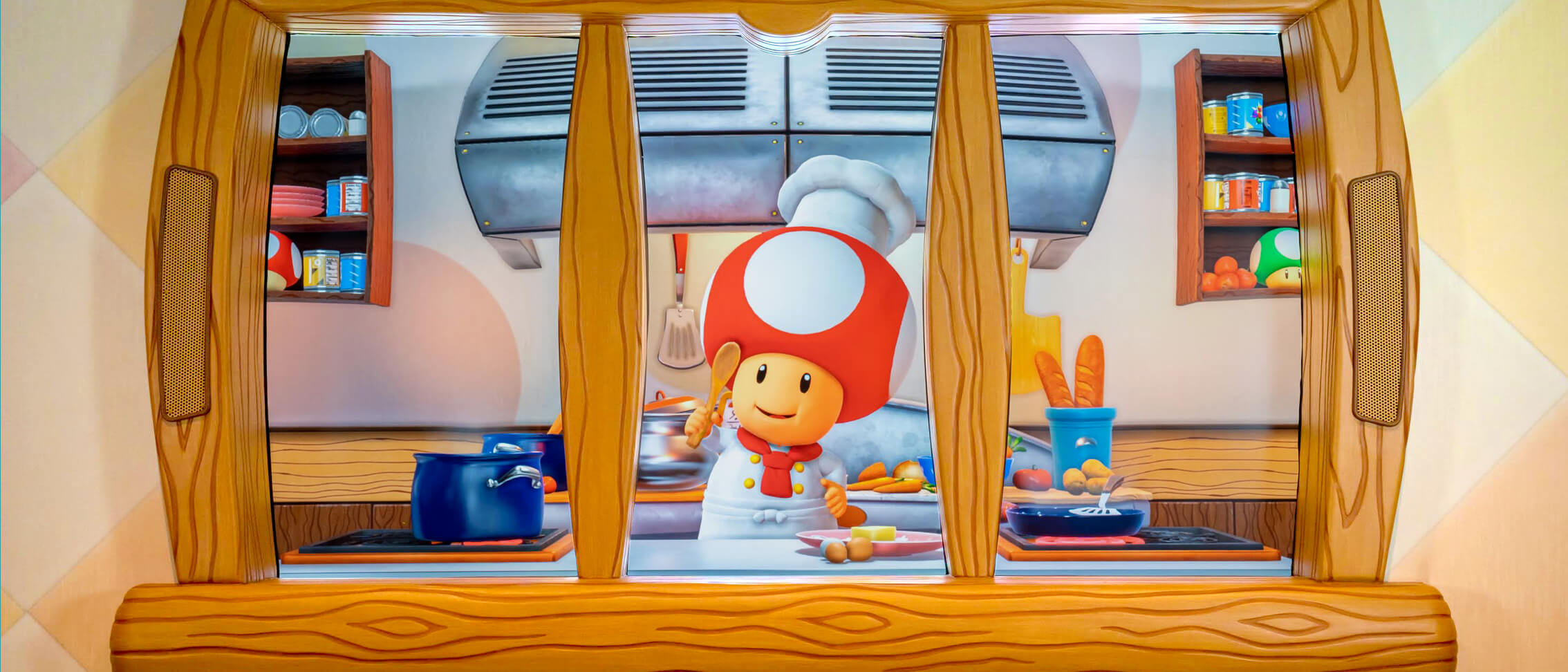 The smiling character Chef Toad, wearing a chef’s coat and hat, stands with a wooden spoon in the window of his kitchen.