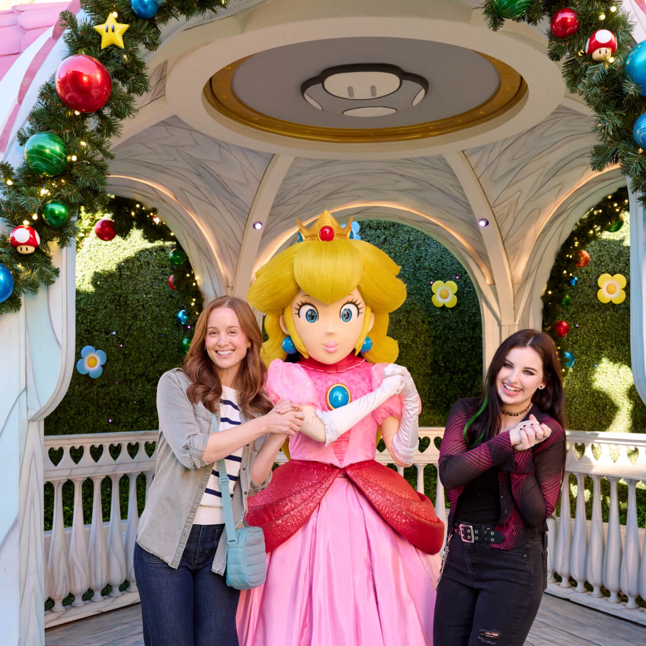 Smiling friends posing for a photo with Princess Peach in her holiday-decorated gazebo.