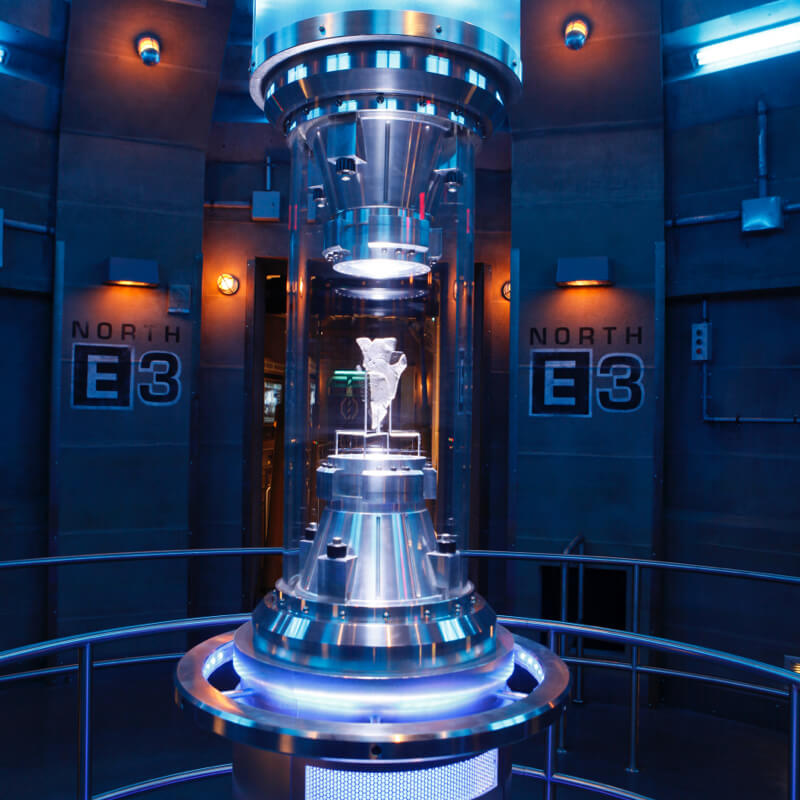 A stone room with a piece of the Allspark in a glass case placed in the middle of the room.