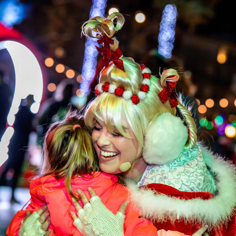 A woman in a fur-trimmed red jacket hugging a little girl.