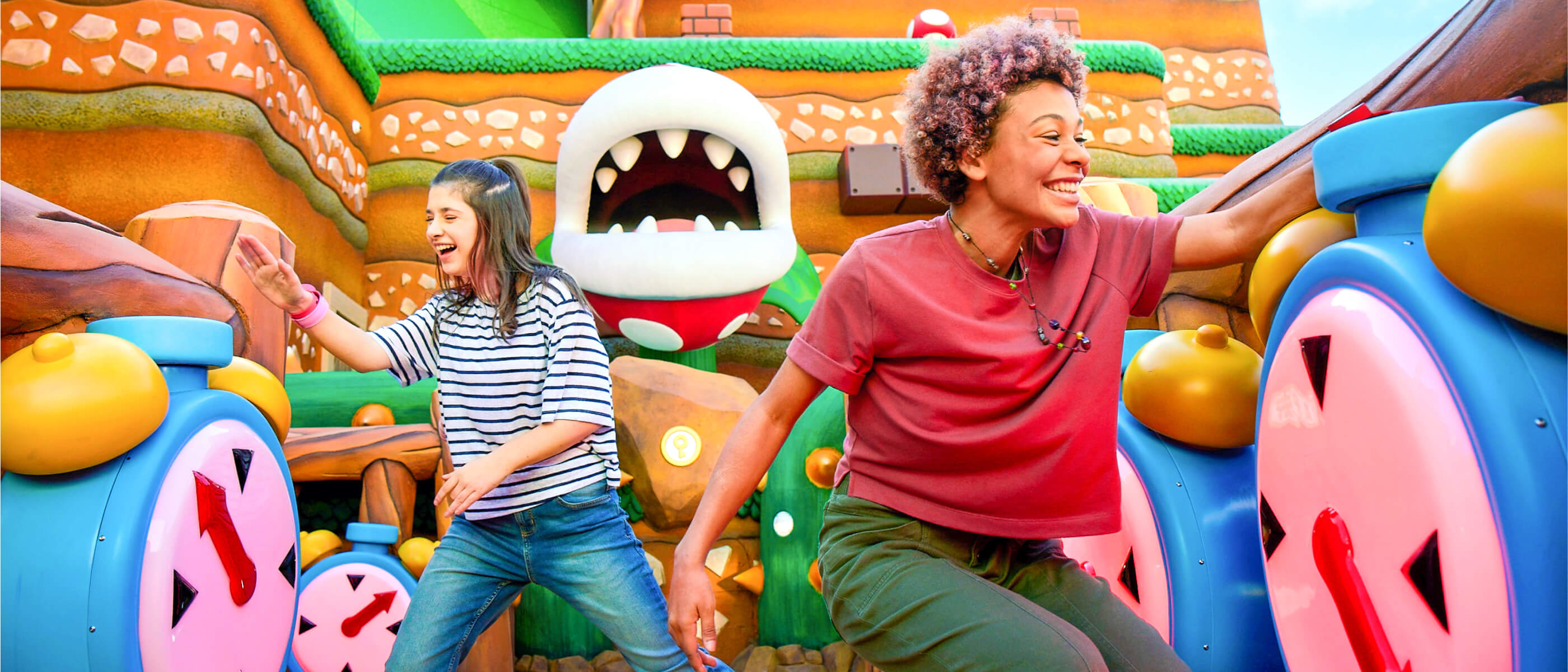 Two excited friends smiling as they tap oversized alarm clocks with Power-Up Bands™ on their wrists in SUPER NINTENDO WORLD™.