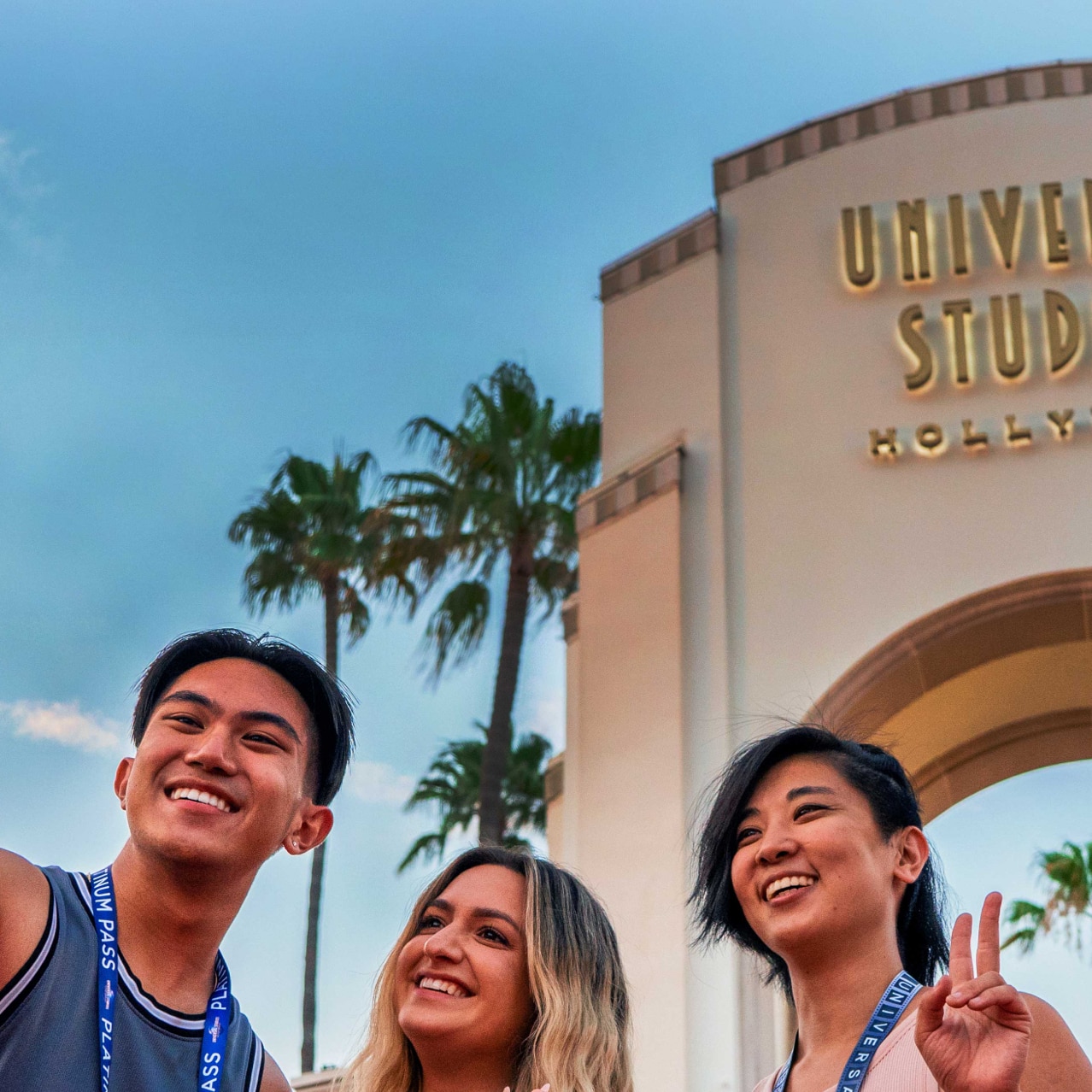 Three Annual Passholder friends take a selfie in front of the iconic Universal Studios Hollywood archway.