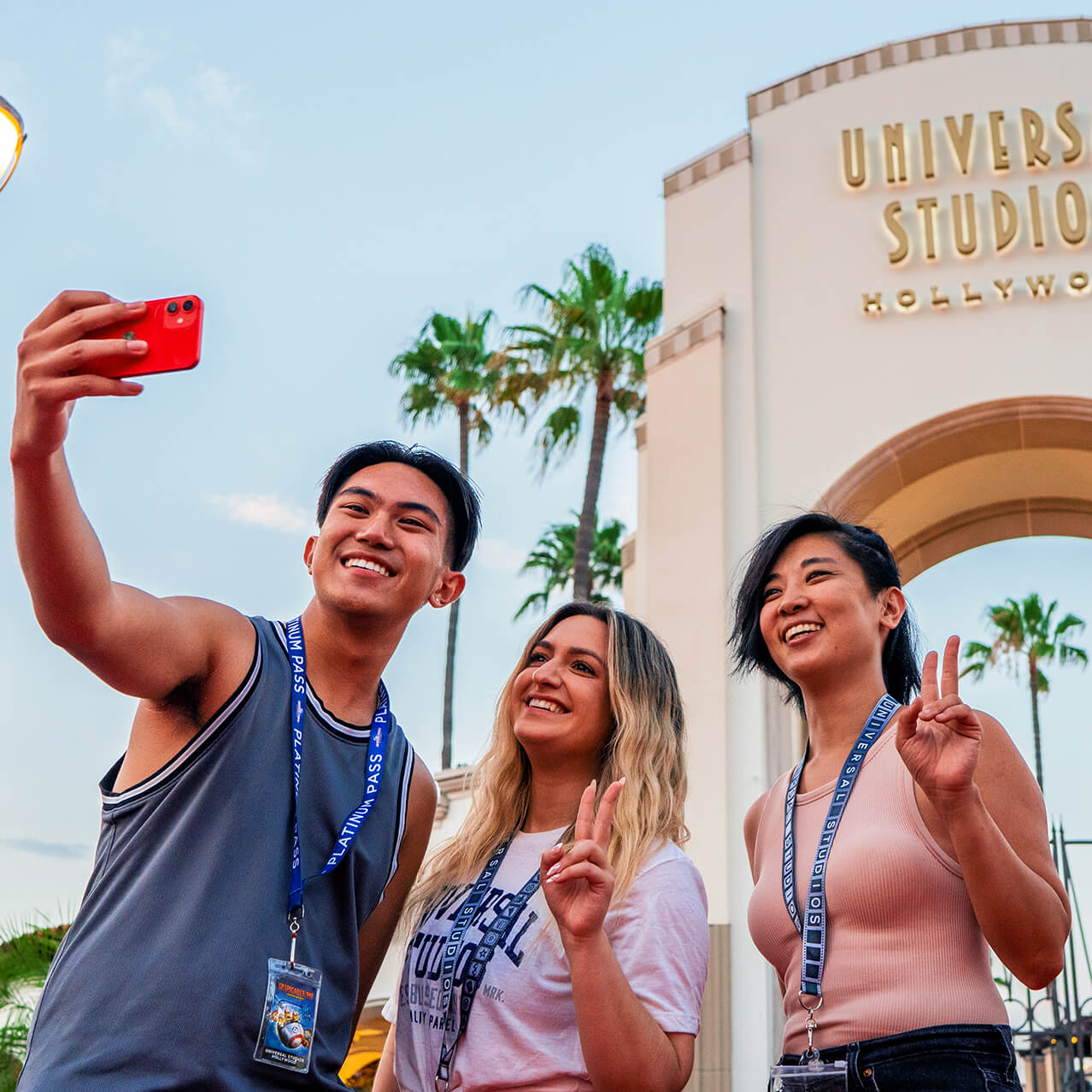 Three Annual Passholder friends take a selfie in front of the iconic Universal Studios Hollywood archway.