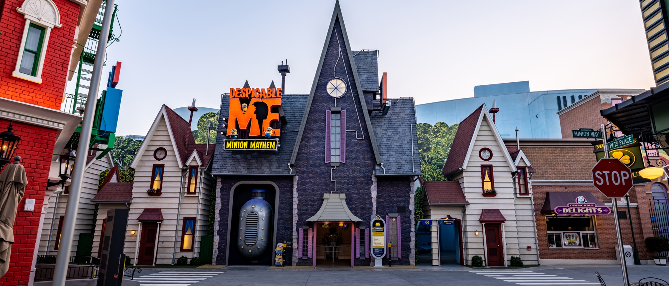 A dark, pointed house with a large metal contraption in an entryway and a “DESPICABLE ME MINION MAYHEM” sign on the roof.