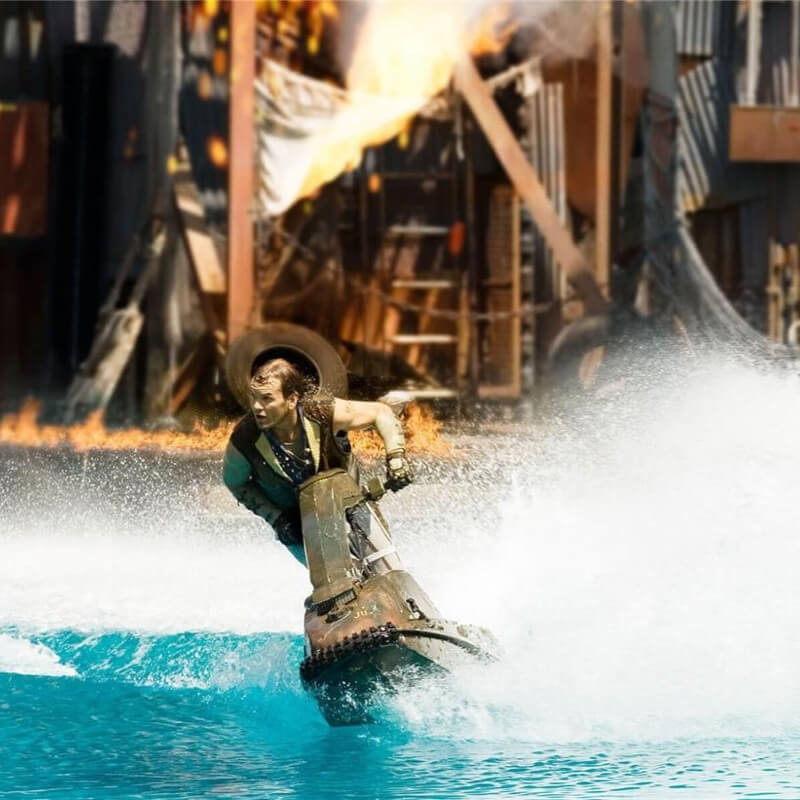 A girl on a jet ski in the water with a building on fire behind.