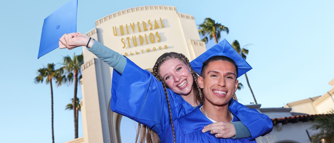 Two students in graduation cap and gowns celebrating in front of the Universal Studios Hollywood entryway arch