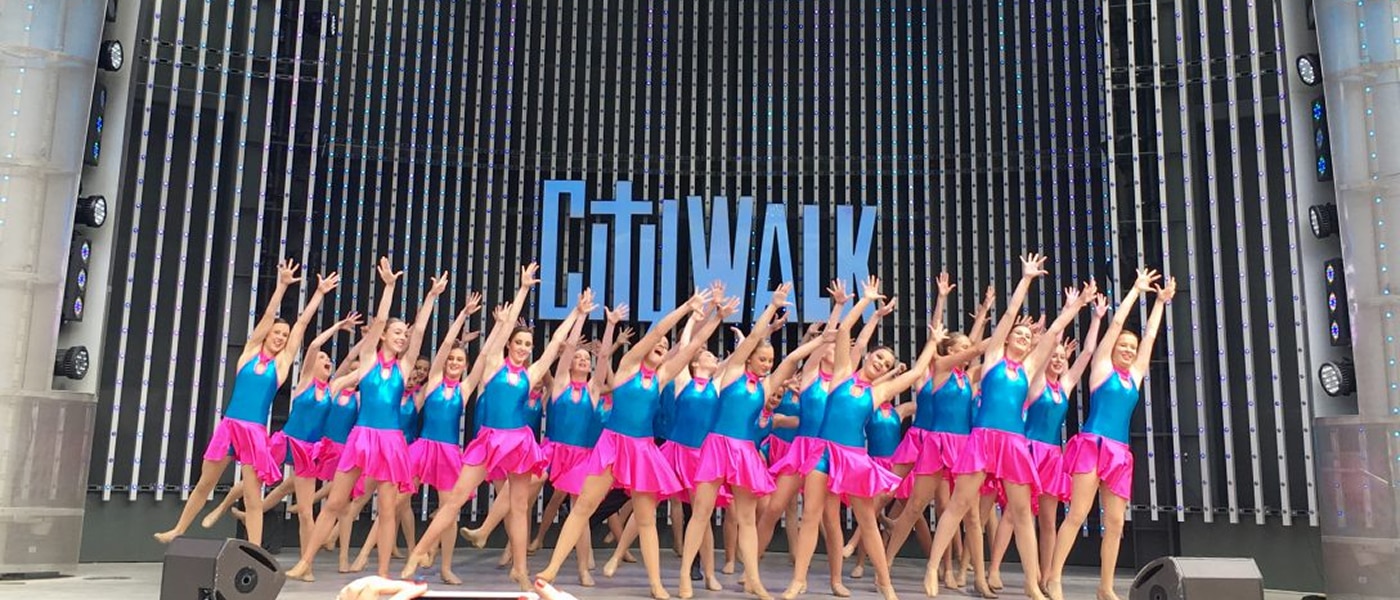 Group of young girls doing a dance performance with their hands in the air in unison on the CityWalk stage