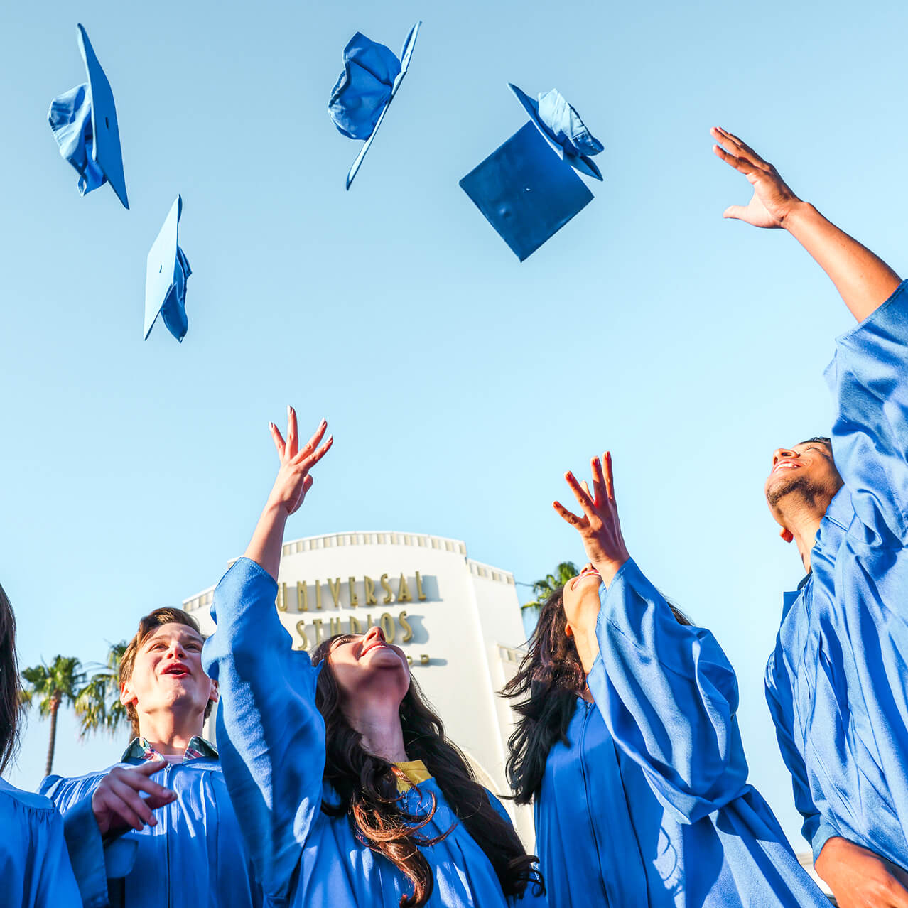 Students in graduation caps and gowns throwing their caps into the air in front of the Universal Studios Hollywood entrance sign