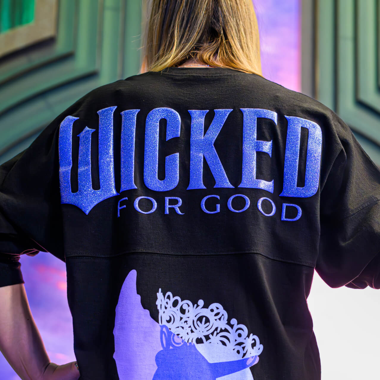 Two models wearing Wicked: For Good merchandise featuring Elphaba and Glinda’s silhouettes.