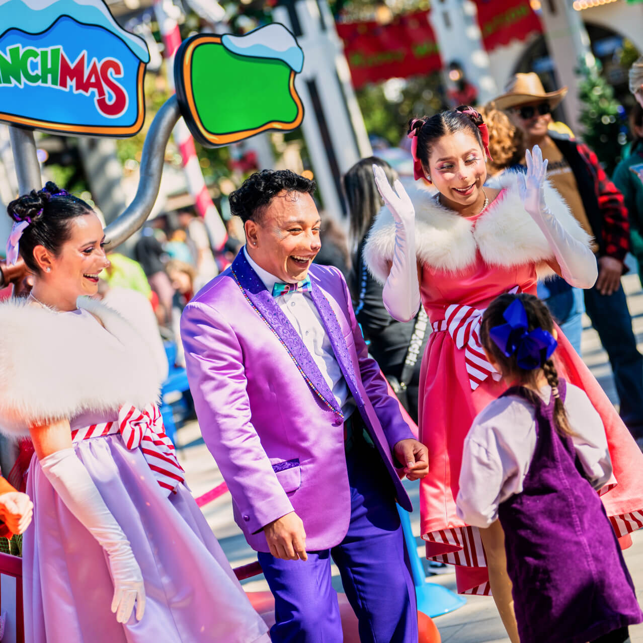 Four Whos from Whoville talking to a young girl in front of a sign that says MERRY GRINCHMAS.