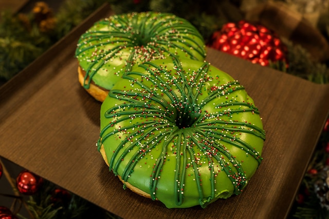 A pair of donuts decorated to look like Christmas wreaths sit on a tray.