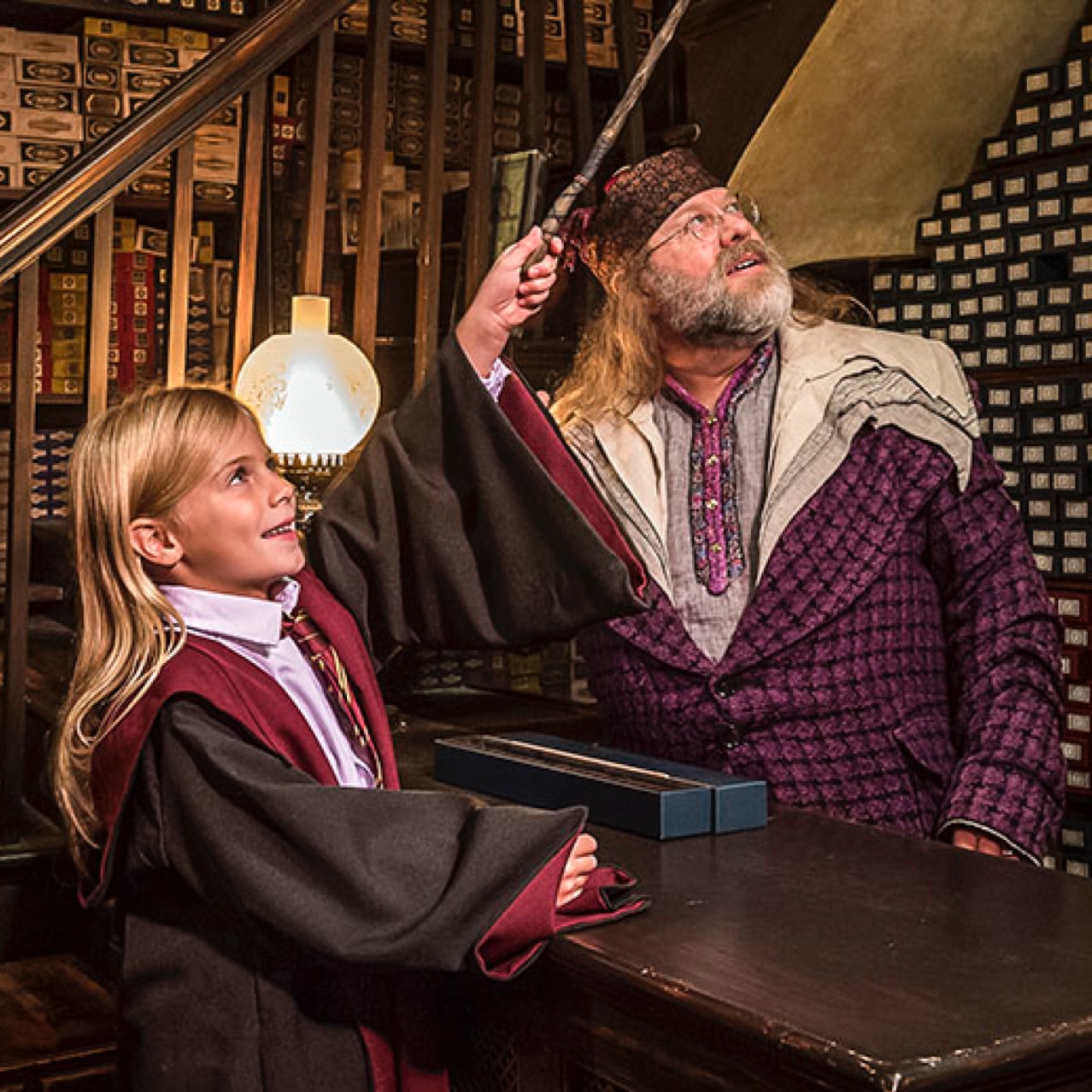 A girl holding a wand and a man looking up in the Ollivanders Wand store.
