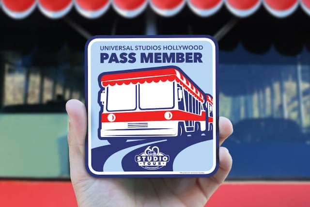 A hand holding up the Studio Tour 60th Anniversary Pass Member tram magnet in front of a Glamor Tram.