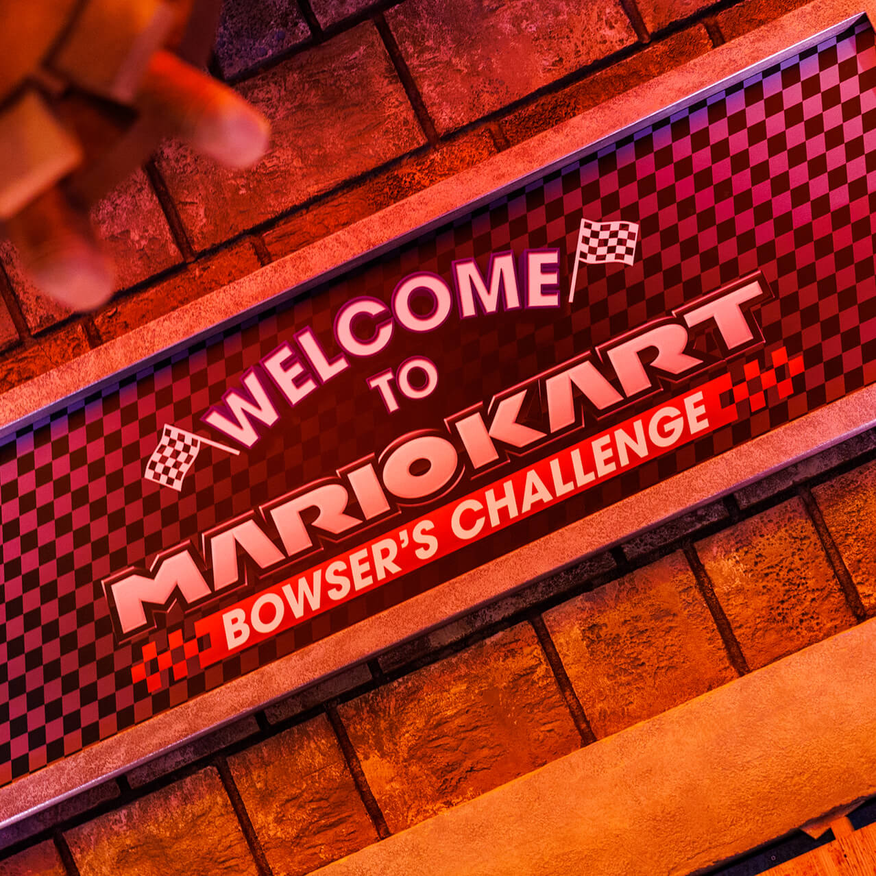 A sign with checkered racing flags in Bowser’s Castle reads: Welcome to Mario Kart: Bowser’s Challenge.
