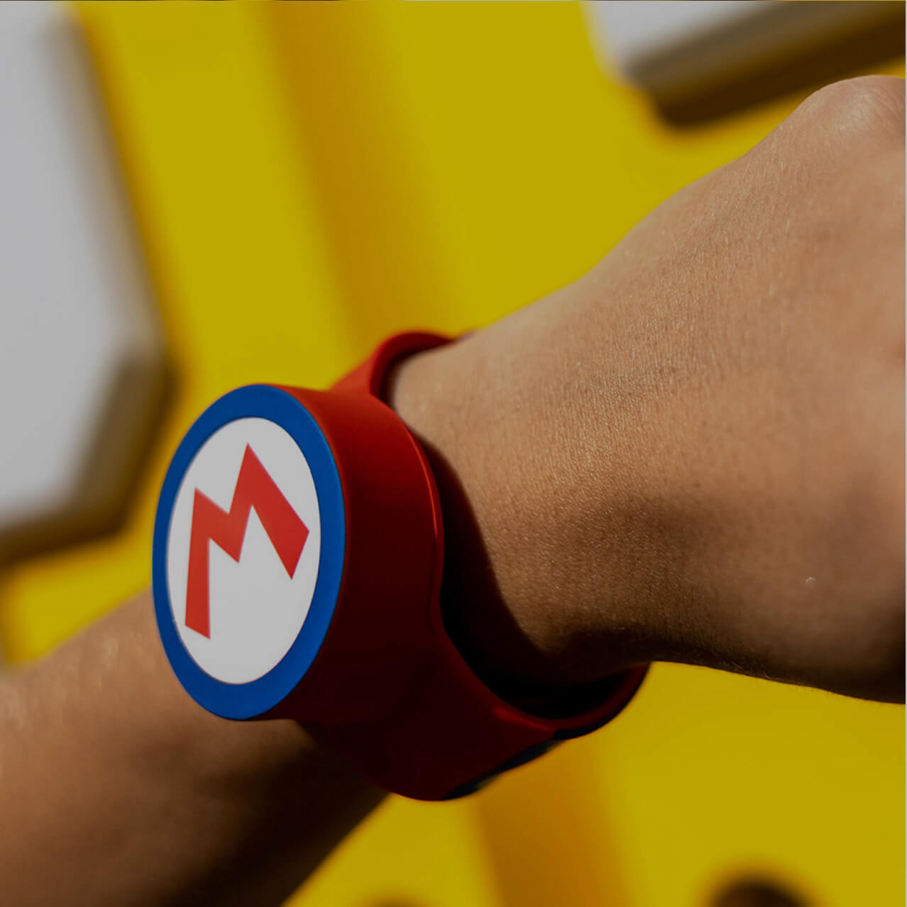 An arm wearing a Power-Up Band on its wrist. On the band is the letter ‘M’ representing the Super Mario character Mario.