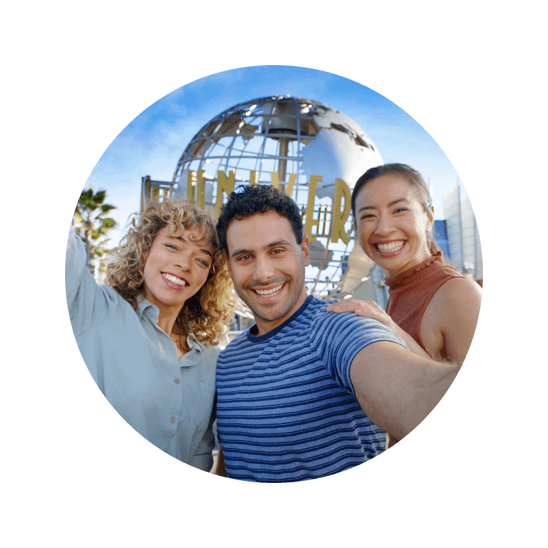 Three happy friends smiling for a selfie in front of the Universal Globe at the entrance to Universal Studios Hollywood.
