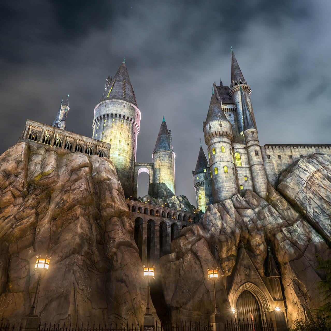 Representación del castillo de Hogwarts iluminado, que se alza imponente sobre su base rocosa en medio de un cielo nocturno brumoso.