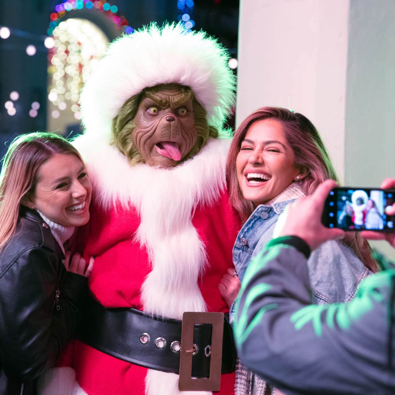 Two women pose with the Grinch sticking out his tongue for a photo.