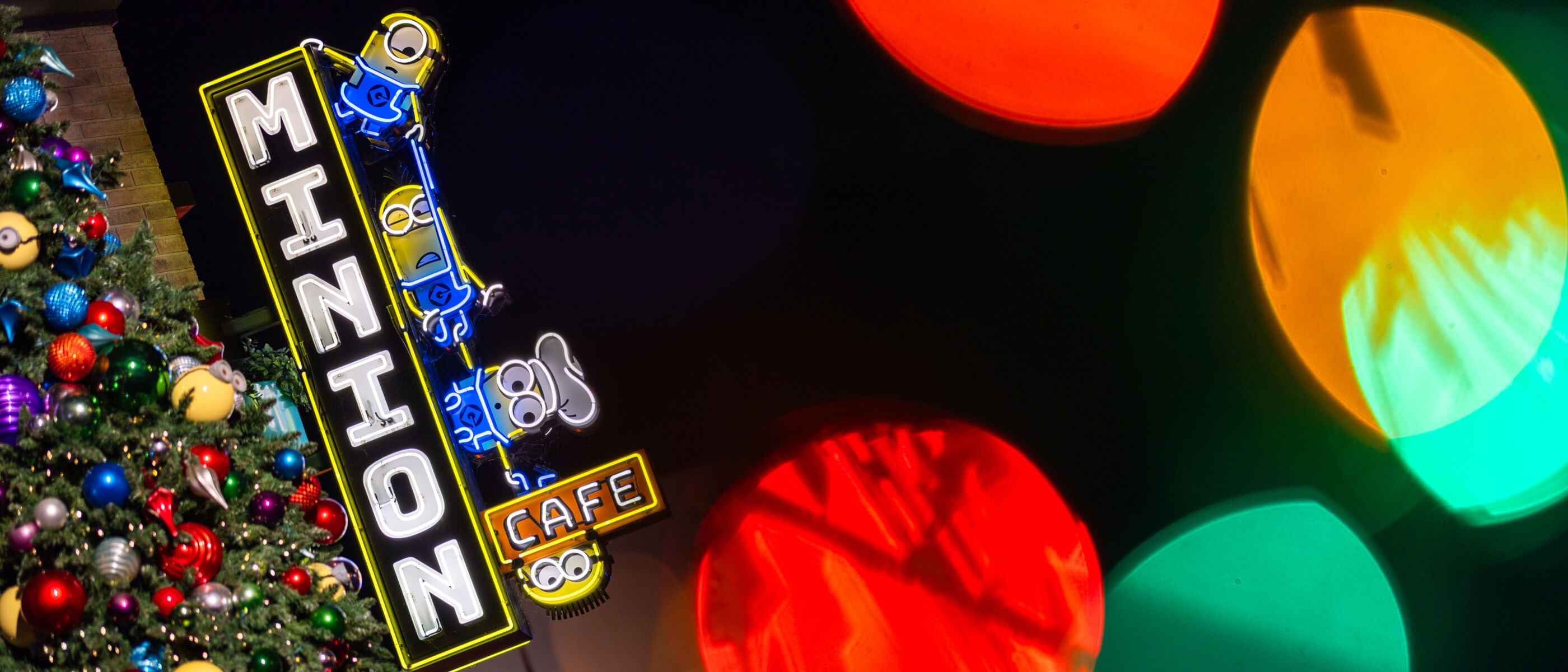 A colorfully decorated Christmas tree next to the Minion Cafe sign at Universal Studios Hollywood.