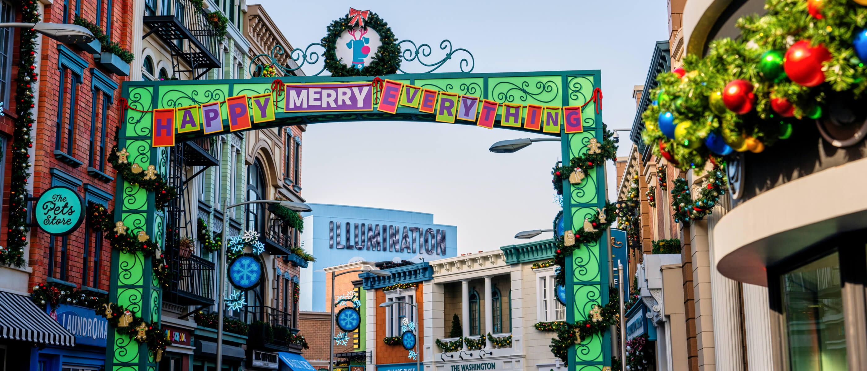 Holiday decor lines the streets with garland and a green archway including a sign that says HAPPY MERRY EVERYTHING.