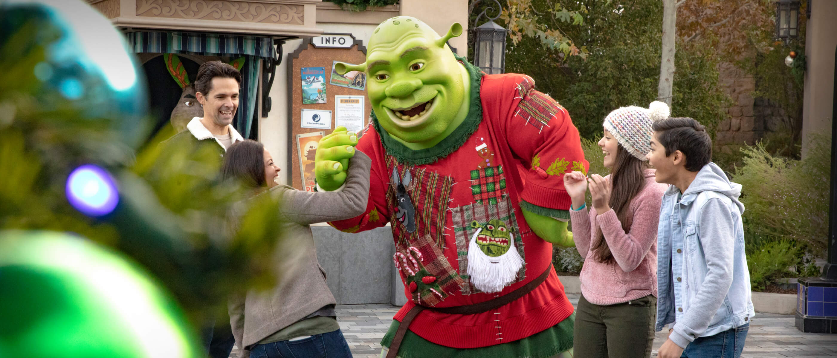 Shrek decked out in a festive, holiday sweater interacting with a family of four during a meet and greet.