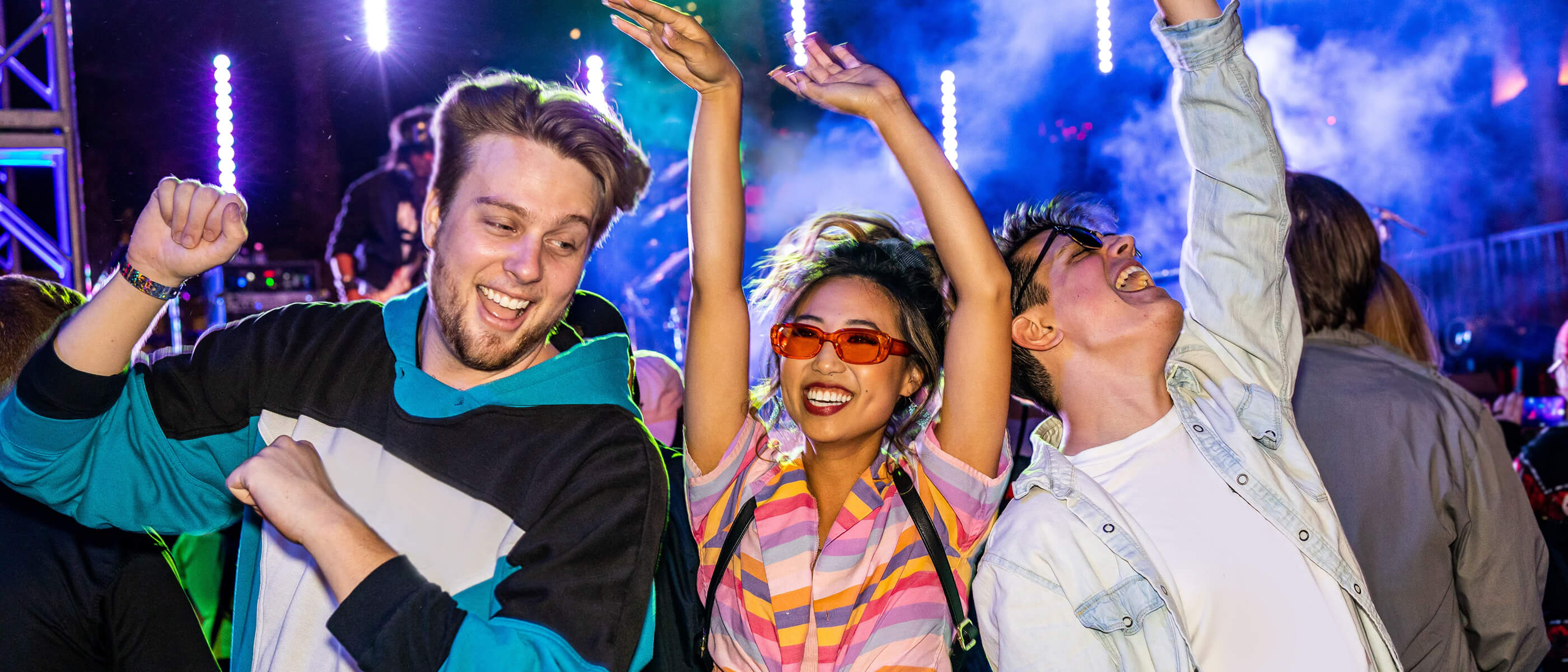Friends dancing together in front of a stage with lights in the background.