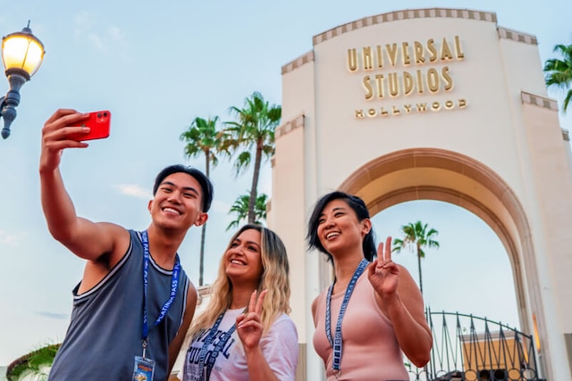 Three Annual Passholder friends pose for a selfie in front of the iconic arch at Universal Studios Hollywood.