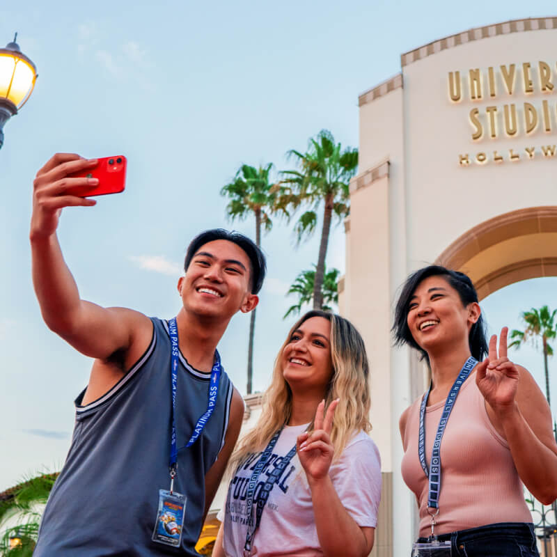 Three Annual Passholder friends pose for a selfie in front of the iconic arch at Universal Studios Hollywood.