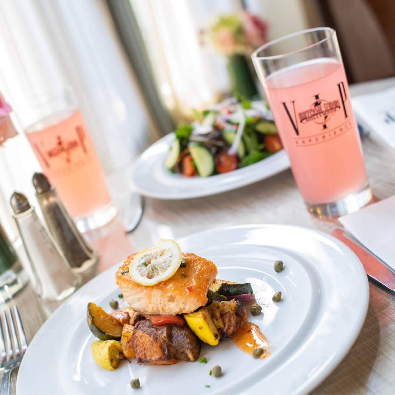 A salmon meal on top of plated vegetables with a pink drink next to the plate. 